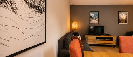 Una sala de estar con un sofá, un televisor, una lámpara e imágenes enmarcadas en la pared.