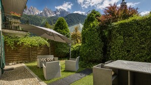 Eine Terrasse mit Korbmöbeln, einem Tisch und einem überdachten Bereich, vor einer Kulisse aus Bergen und Bäumen.