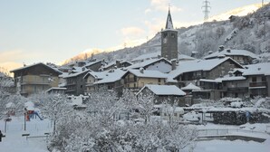 Un poble cobert de neu amb edificis tradicionals, una torre d'església i un teleàsptic al fons.