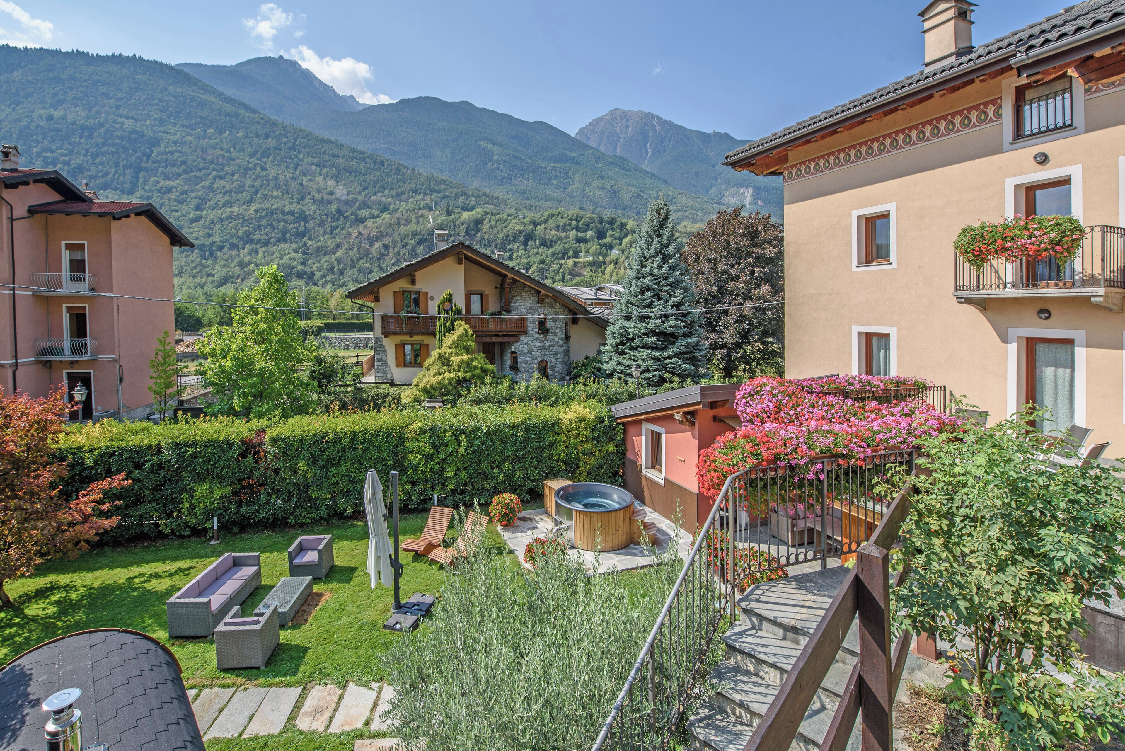 A residential area with a mountain backdrop, featuring a house with a stone facade, a wooden deck, and a hot tub.