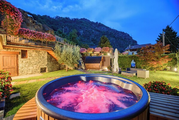 A hot tub in a garden with a stone building and a mountain in the background. - Mountain villa for families / groups (4-16 guests) (Chambave)