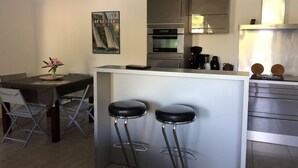 A compact kitchen with a central island, bar stools, a dining table with chairs, and a poster on the wall. - Apartment/ flat - Cassis (Cassis)