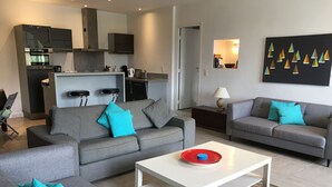 A modern living room with grey sofas and teal cushions, a white coffee table, and a kitchen in the background. - Apartment/ flat - Cassis (Cassis)