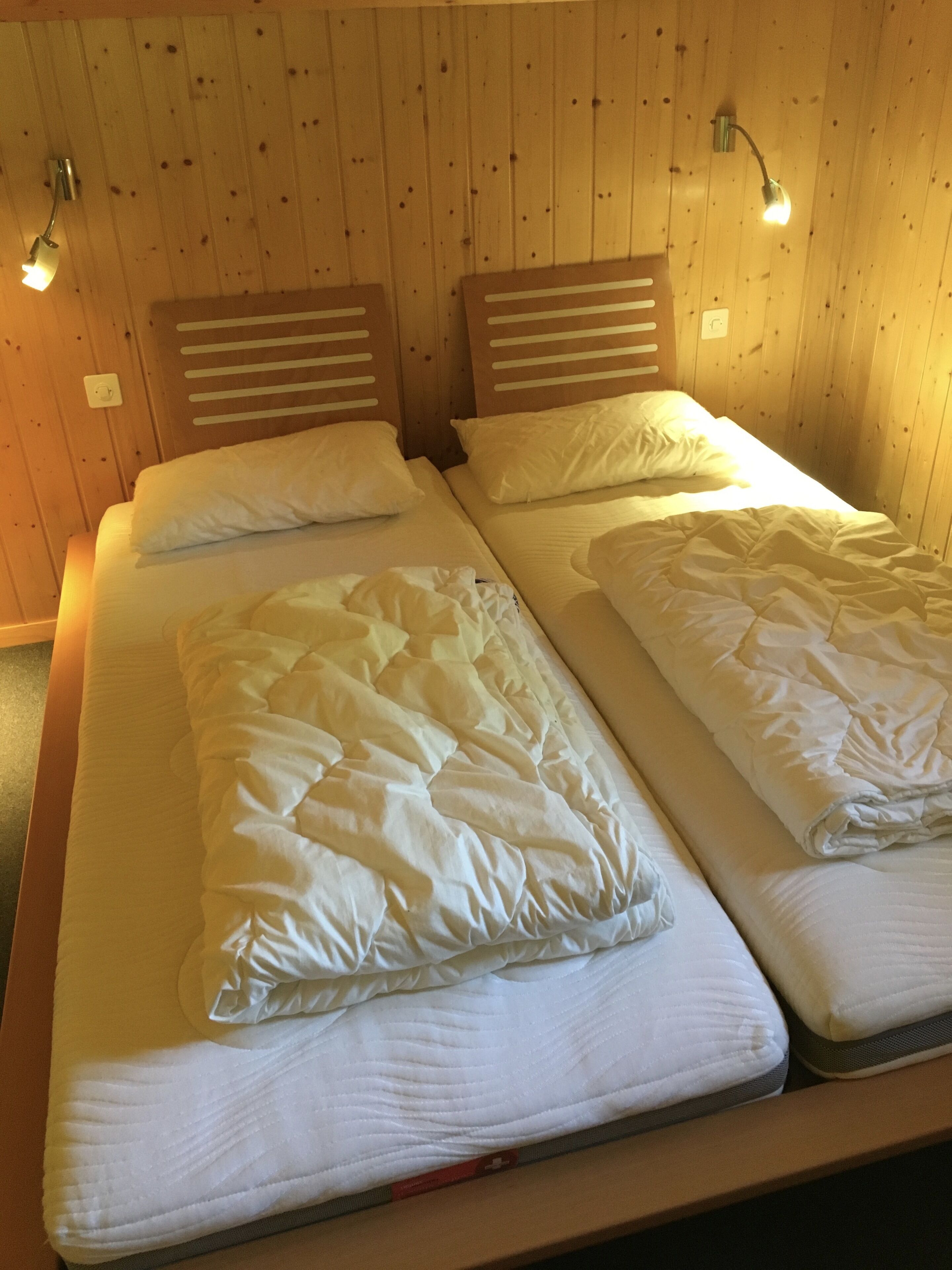 A double bed with a quilted duvet and two pillows, wooden headboards, and bedside lamps.