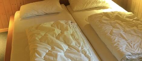 A double bed with a quilted duvet and two pillows, wooden headboards, and bedside lamps.