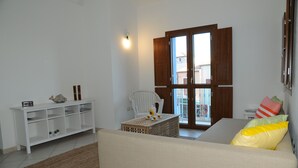 Un salon comprenant un canapé, un fauteuil blanc, une petite table agrémentée d’objets décoratifs, une console blanche et une porte en bois avec des panneaux de verre.