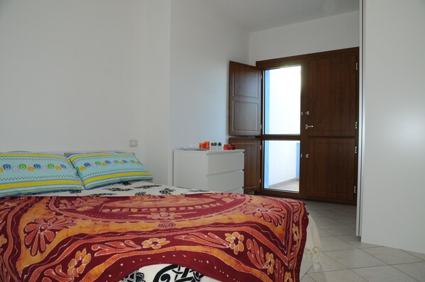 Une chambre à coucher avec un lit, des oreillers, une table de chevet, une armoire et une fenêtre.