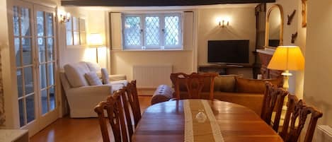 A cozy living room with a wooden dining table, comfortable seating, a TV, and a window with a view.