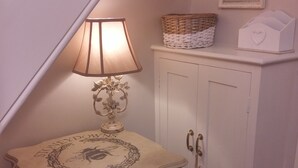 Et lille bord med en lampe, en fletkurv og et velkomstskilt i ramme på væggen.