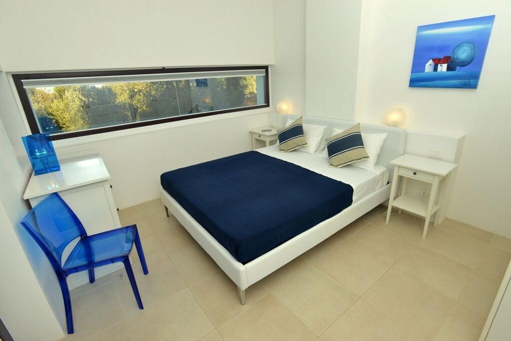 A bedroom with a bed, a desk, a chair, a window, and a painting on the wall.