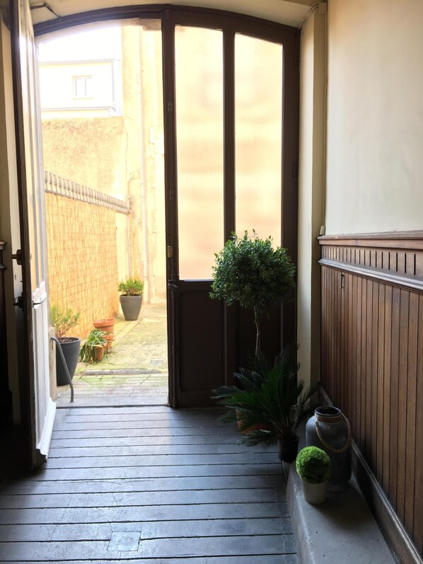 Une porte en bois qui donne sur une cour intérieure agrémentée de plantes en pot et d’une petite table.