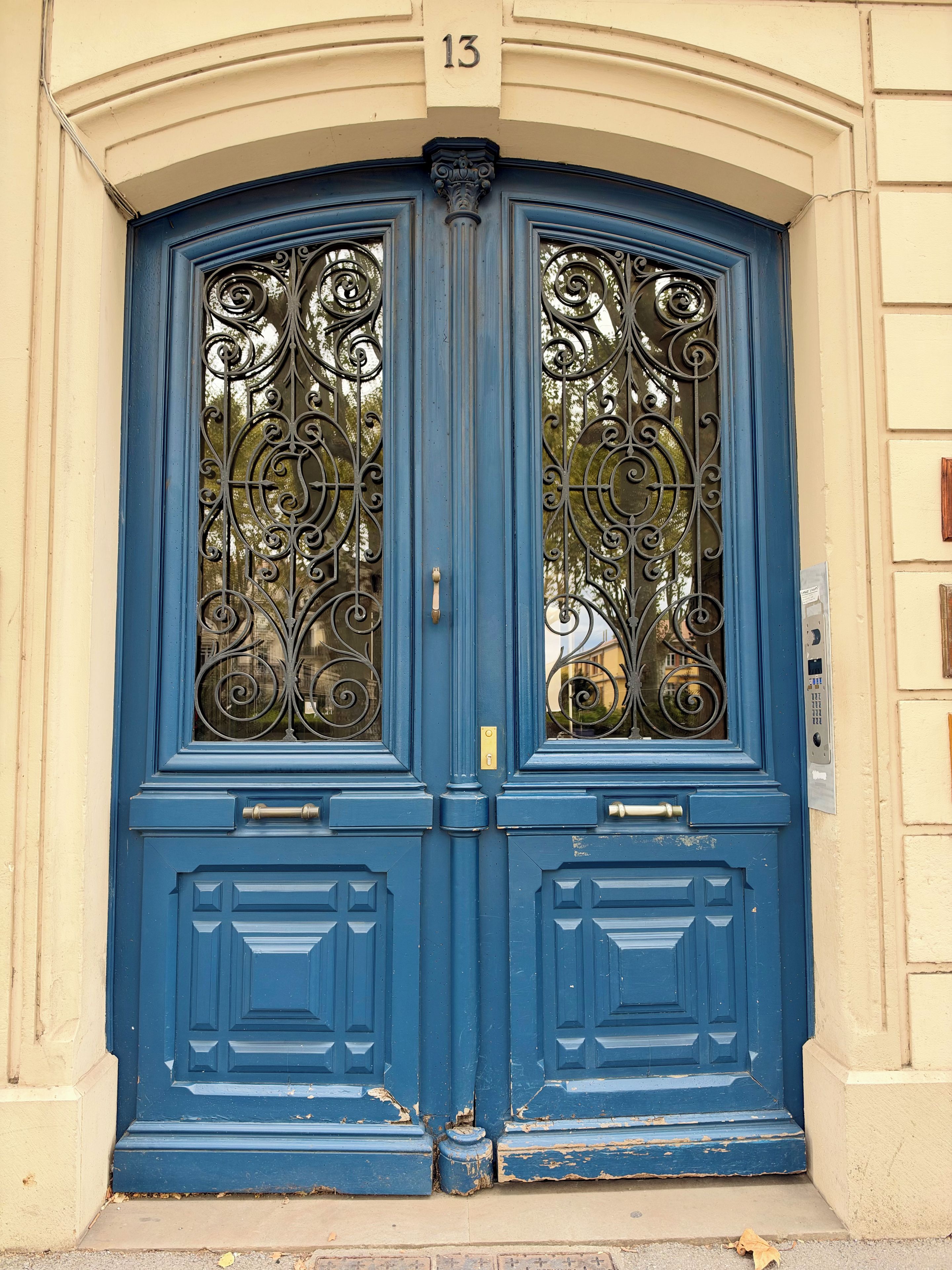 A blue double door with ornate ironwork and a brass handle.