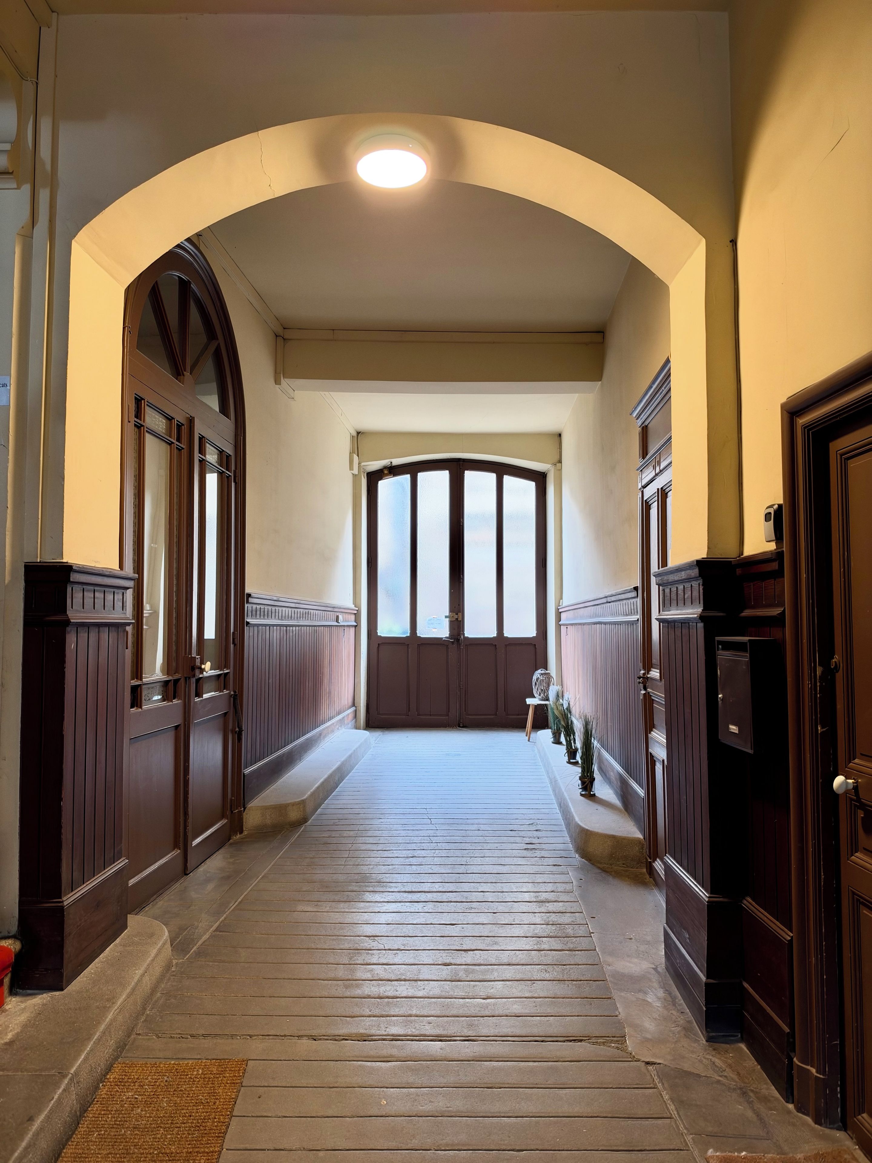 Un pasillo con piso de madera, una puerta central e iluminación en el techo.