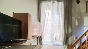 Eine kleine Küche mit Fernseher, Schränken und einem Fenster mit durchsichtigen Vorhängen.