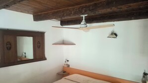 Ein Schlafzimmer mit Bett, Deckenventilator, Spiegel und einer kleinen Ablagefläche.