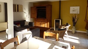 A living room with a sofa, a television, a fireplace, and a dining area with chairs and a table. - Holiday house at 800m from the beach in De Haan (De Haan)