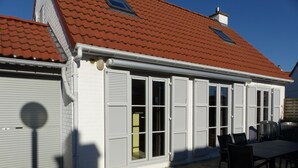 A building with a red-tiled roof, white exterior walls, and a covered patio area with a table and chairs. - Holiday house at 800m from the beach in De Haan (De Haan)
