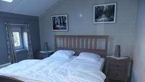 A bedroom with a wooden bed, two nightstands, a window with curtains, and two framed pictures on the wall. - Holiday house at 800m from the beach in De Haan (De Haan)