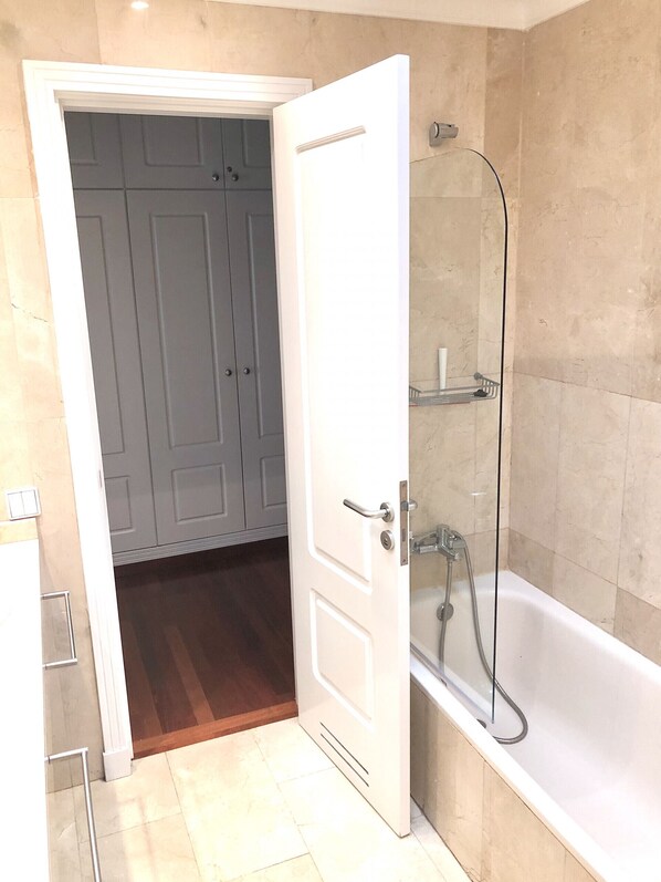Un baño con bañera, ducha y una puerta que da a un cuarto con armarios.