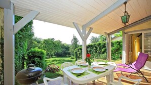 Un patio al aire libre con una mesa lista para comer, rodeada de sillas y una parrilla.