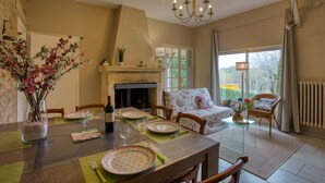 Un área de comedor con chimenea, una mesa de comedor con platos y vasos, y una silla con cojín floral.