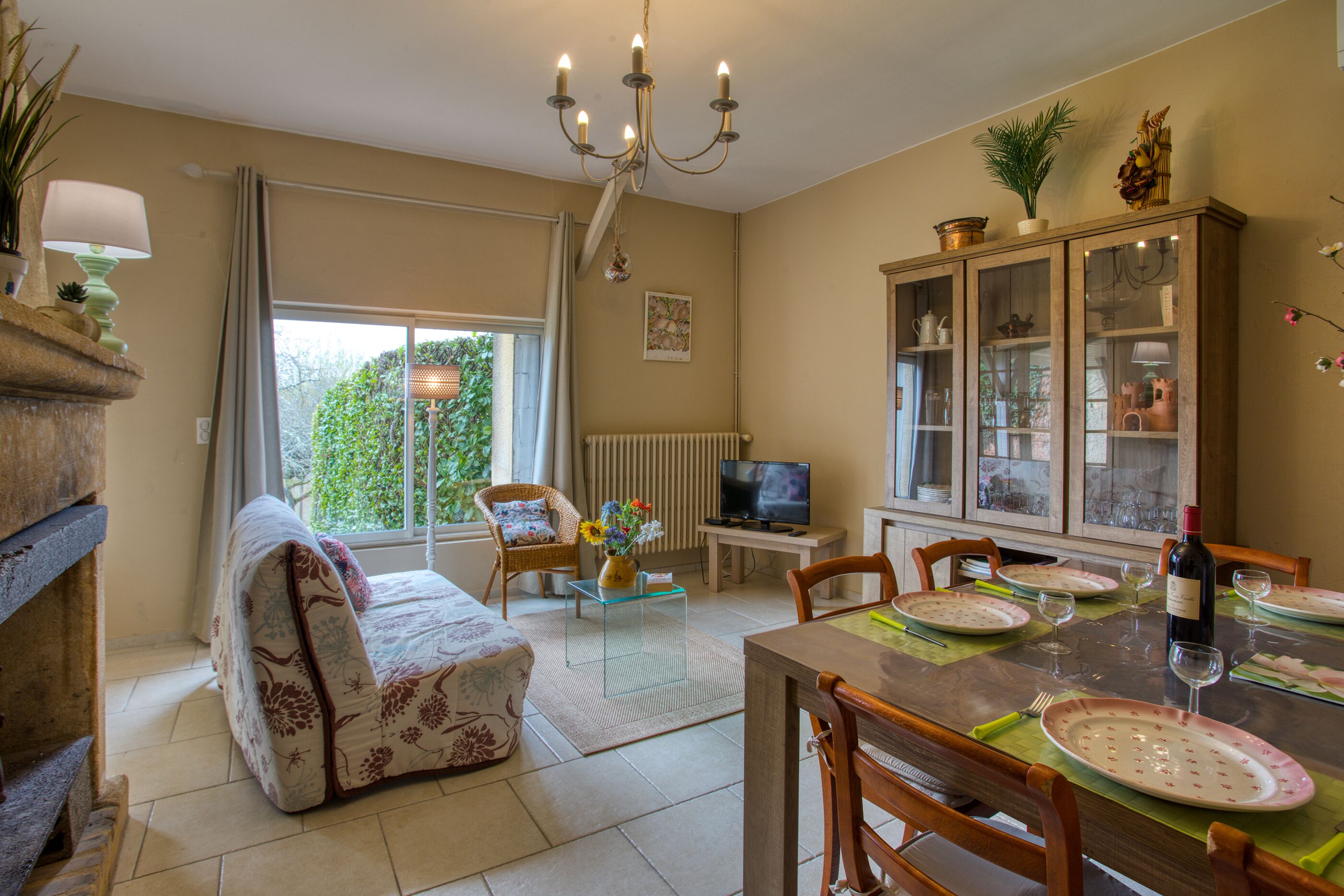 A dining area with a table set for four, a sofa, a television, and a cabinet with glass doors.