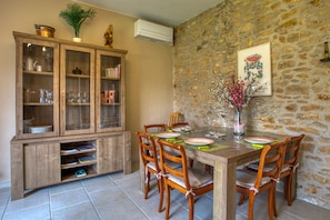 Un comedor con pared de piedra, un mueble de madera con puertas de cristal y una mesa dispuesta para cuatro personas.