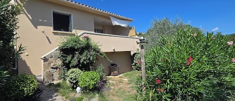 A two-story house with a beige exterior, a stone wall, and a garden with various plants and flowers.