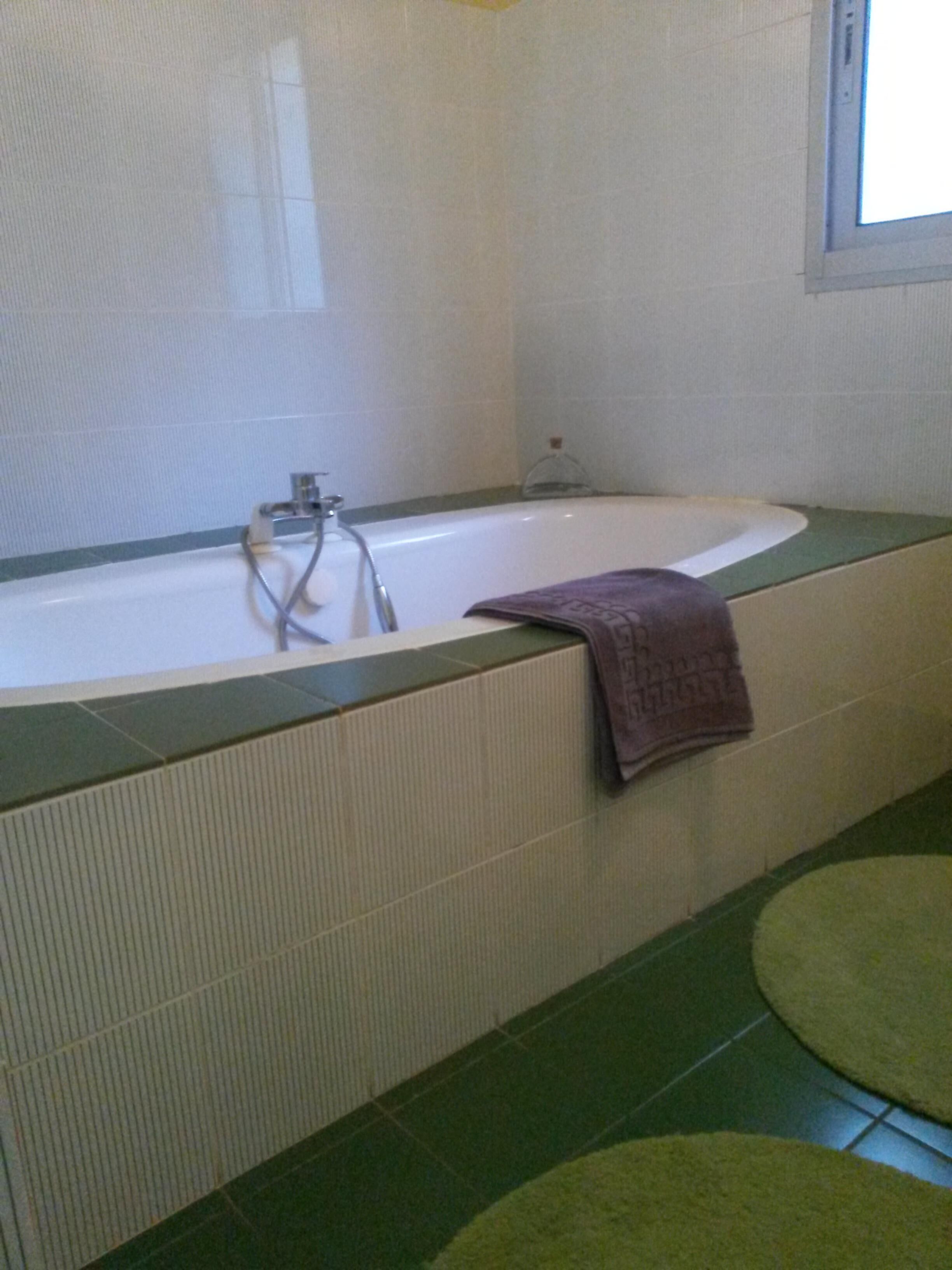 Casa de banho com banheira, paredes azulejadas em tons de verde e branco e uma janela.