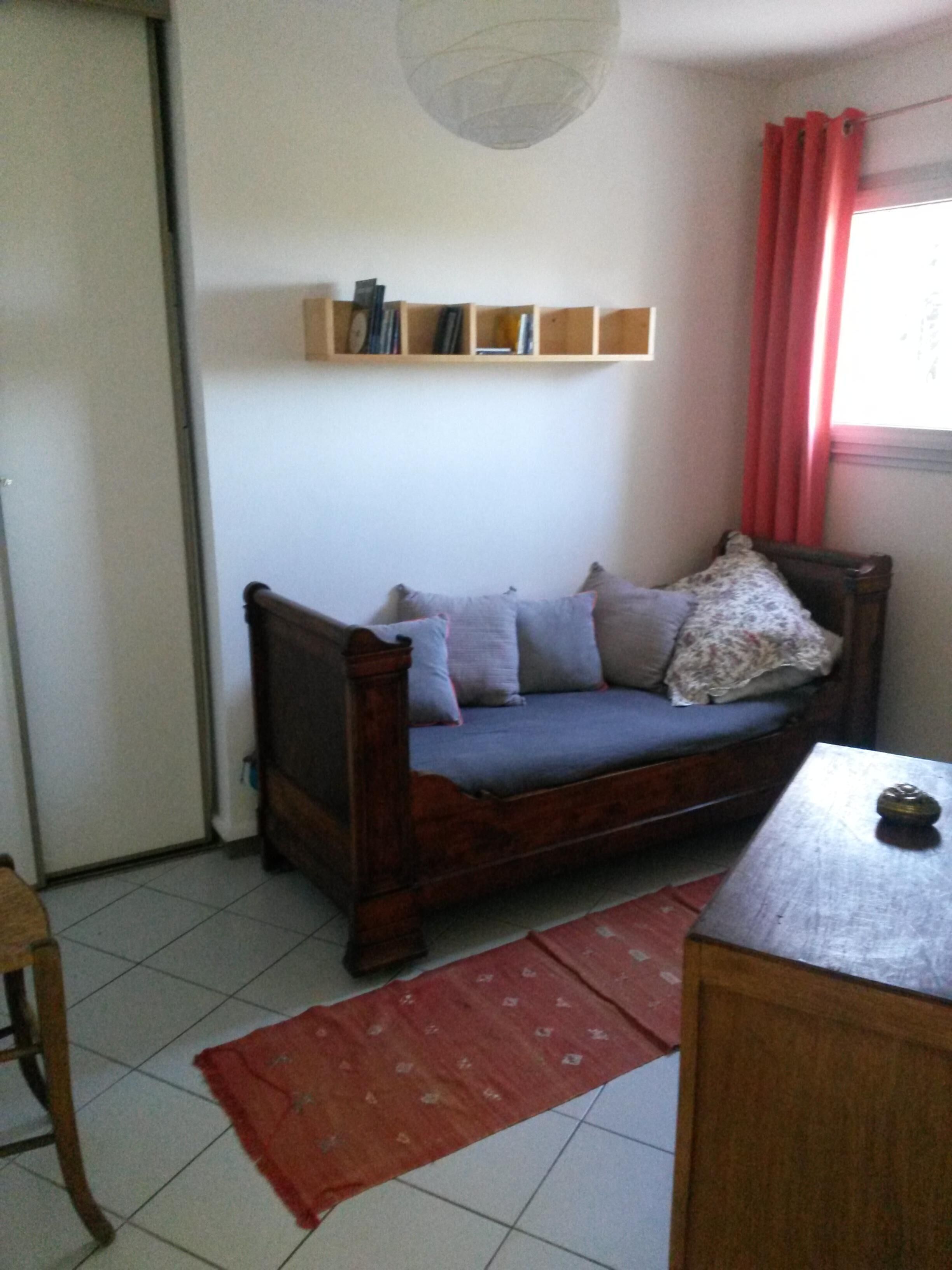 A room with a wooden sofa, a red rug, a small wooden table, and a window with red curtains.