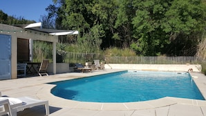 A swimming pool with a curved edge, surrounded by a patio area with lounge chairs and a small table. - Villa with swimming pool, located in the heart of the Catalan garrigue. (Millas)