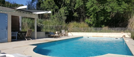 A swimming pool with a curved edge, surrounded by a patio area with lounge chairs and a small table.