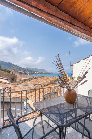 A terrace with a metal table and chairs, overlooking a coastal landscape with buildings and the sea.