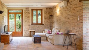 A cozy room with a brick wall, a wooden door, a sofa, a small table, and a floor lamp. - Villa Lucia with pool in the Marche region, elegant and spacious, a few kilometers from the Adriatic (Barchi)