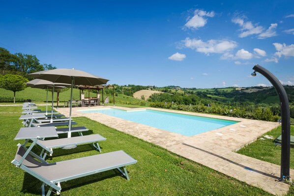 A poolside area with lounge chairs, a pergola, and a view of rolling hills. - Villa Lucia by Anita Villas (Barchi)