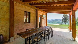 A covered patio with a wooden table and chairs, brick walls, and a view of the countryside. - Villa Lucia with pool in the Marche region, elegant and spacious, a few kilometers from the Adriatic (Barchi)