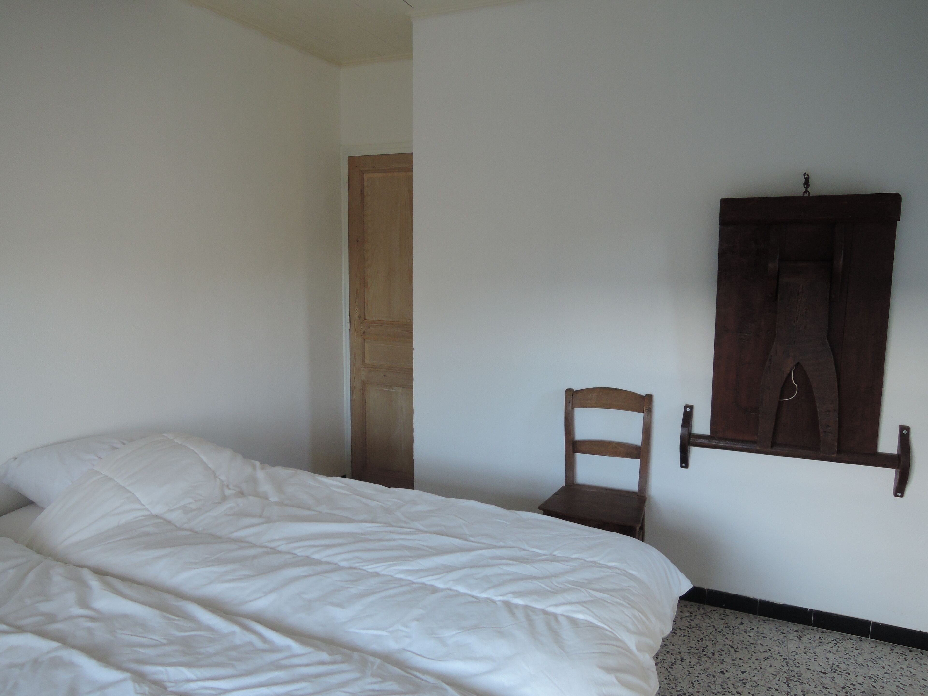 A bedroom with a bed, a wooden chair, a wooden wardrobe, and a door.