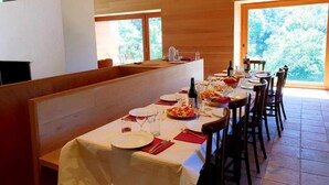 A dining area with a long table set for a meal, wooden walls, and large windows offering a view of trees. - Rural house in an impressive natural setting! Up to 10 people (Montagut I Oix)