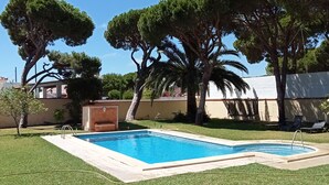A swimming pool surrounded by well-maintained grass and trees, with a clear blue sky above. - Villa with private pool, barbecue and WIFI near the beach. (Chiclana de la Frontera)