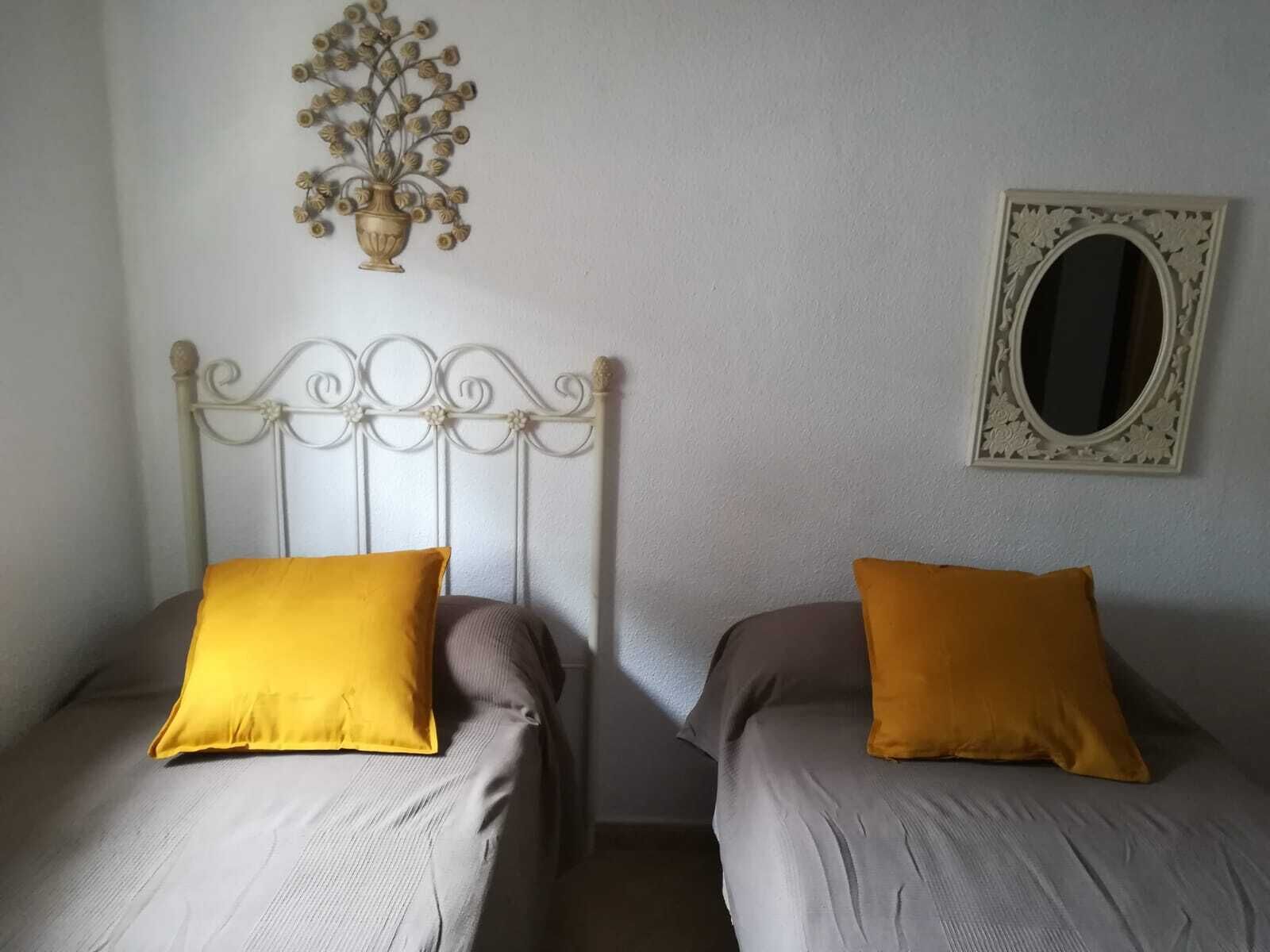 Dos camas individuales con cabeceras y almohadas a juego, un espejo fijado a la pared y una pieza decorativa en la pared.