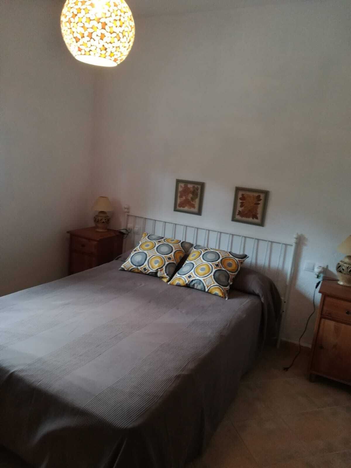 A bedroom with a bed, two pillows, a nightstand, a lamp, and two wall-mounted pictures.