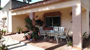 A covered patio with a table and chairs, surrounded by potted plants. - Villa with private pool, barbecue and WIFI near the beach. (Chiclana de la Frontera)