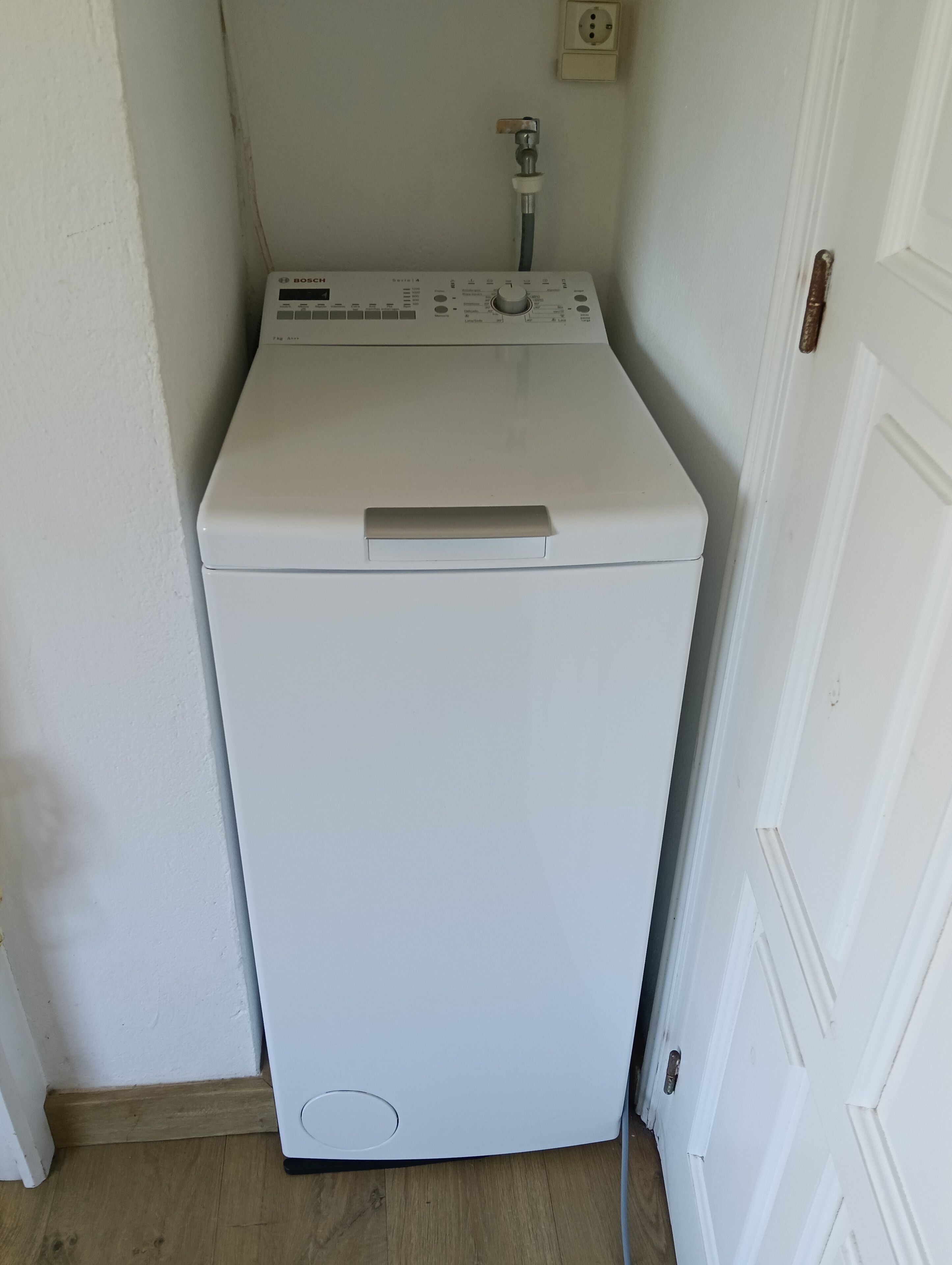 A white washing machine in a corner with a wooden floor and a white door.