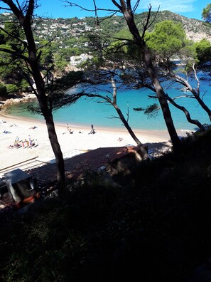 A beach with clear blue water, people sunbathing, and buildings in the background.