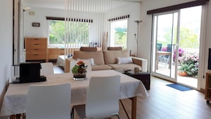 A spacious living room with a sofa set, a dining table with chairs, a ceiling fan, and large windows offering a view of the outdoors. - Loft in Aiguablava beach. Costa Brava. With private garden and sea views. (Begur)