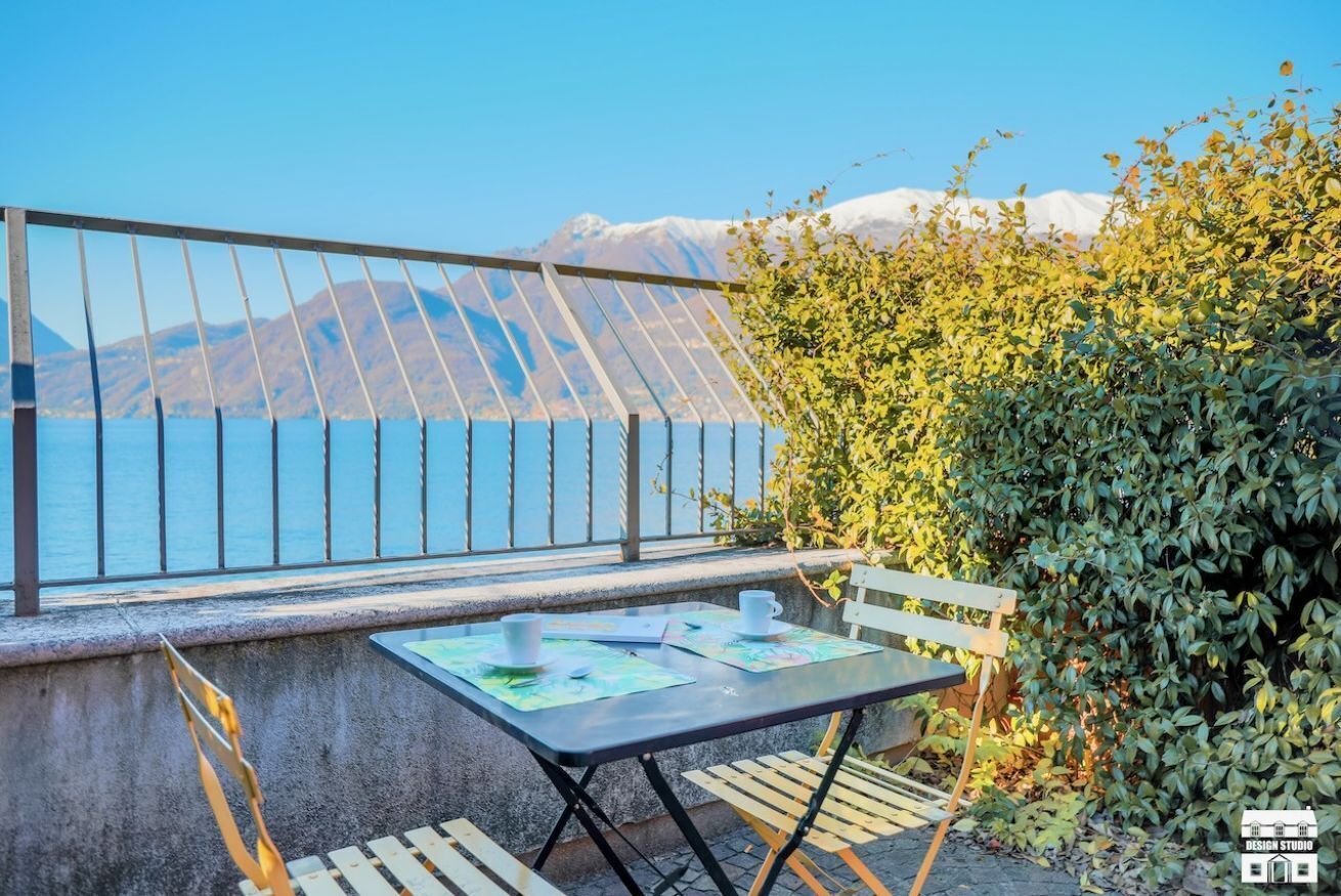 Un balcón con mesa y sillas, con vista a un cuerpo de agua y montañas.