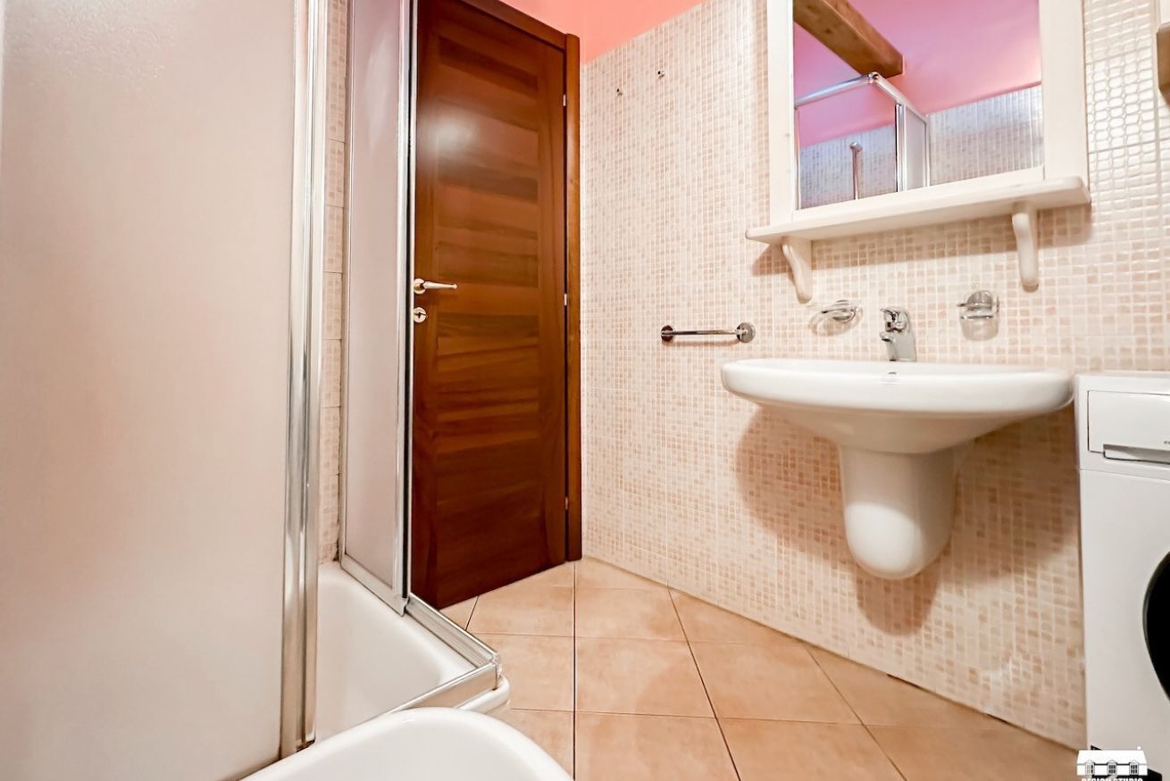 Une salle de bain avec une porte en bois, un lavabo blanc et un sol carrelé.