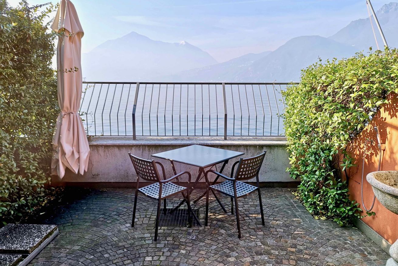 Eine Terrasse im Freien mit Tisch und Stühlen, Blick auf das Meer und einem Bergpanorama.