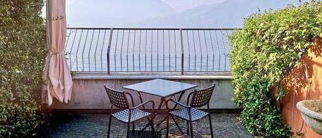 Eine Terrasse im Freien mit Tisch und Stühlen, Blick auf das Meer und einem Bergpanorama.