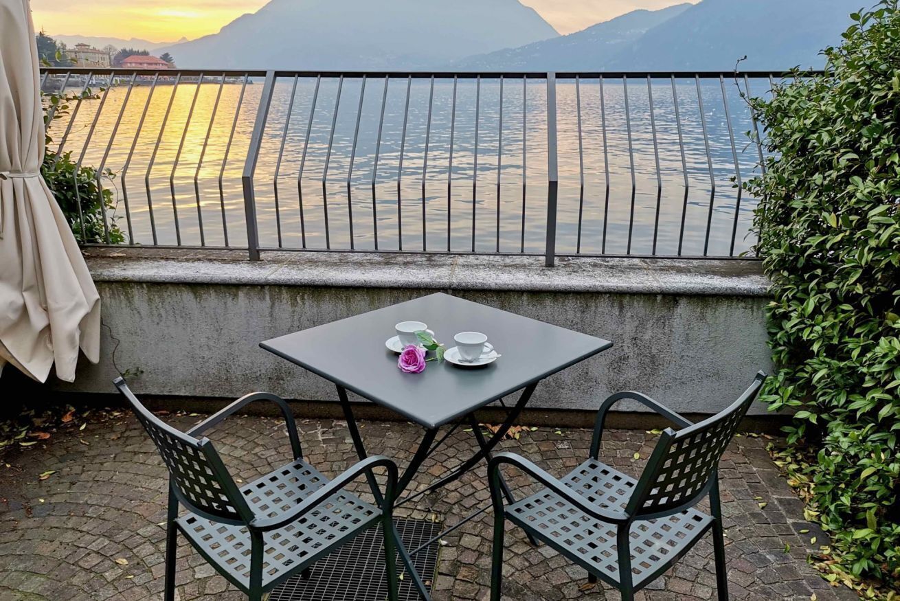 Une terrasse avec une table dressée pour deux personnes, offrant une vue sur un plan d’eau et des montagnes.